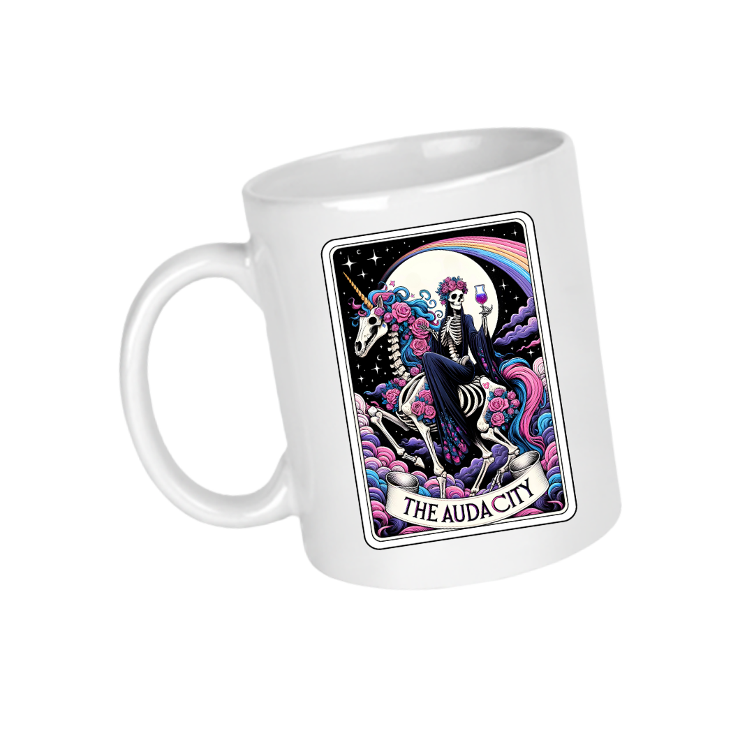 A ceramic mug with a colourful tarot card style design featuring a skeleton riding a skeleton unicorn and text that reads 'AUDACITY'.