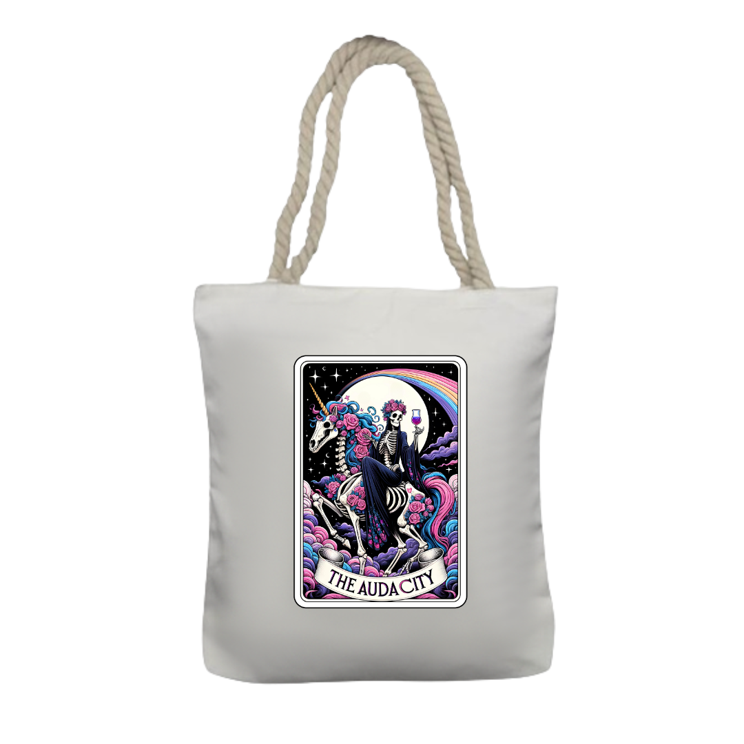 A white tote bag with thick twisted rope handles featuring a colourful tarot card style design with a skeleton riding a skeleton unicorn and the text 'AUDACITY'.