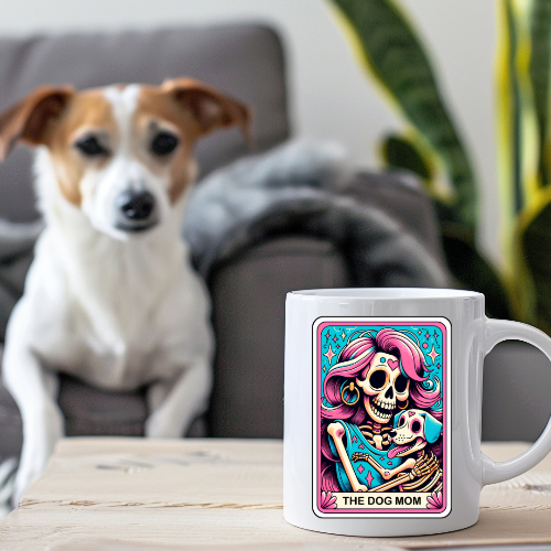 White mug with colorful design featuring a skeleton and dog, placed on a table with a dog sitting in the background.