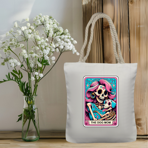 Tote bag with 'The Dog Mom' design next to a vase of white flowers on a wooden surface.